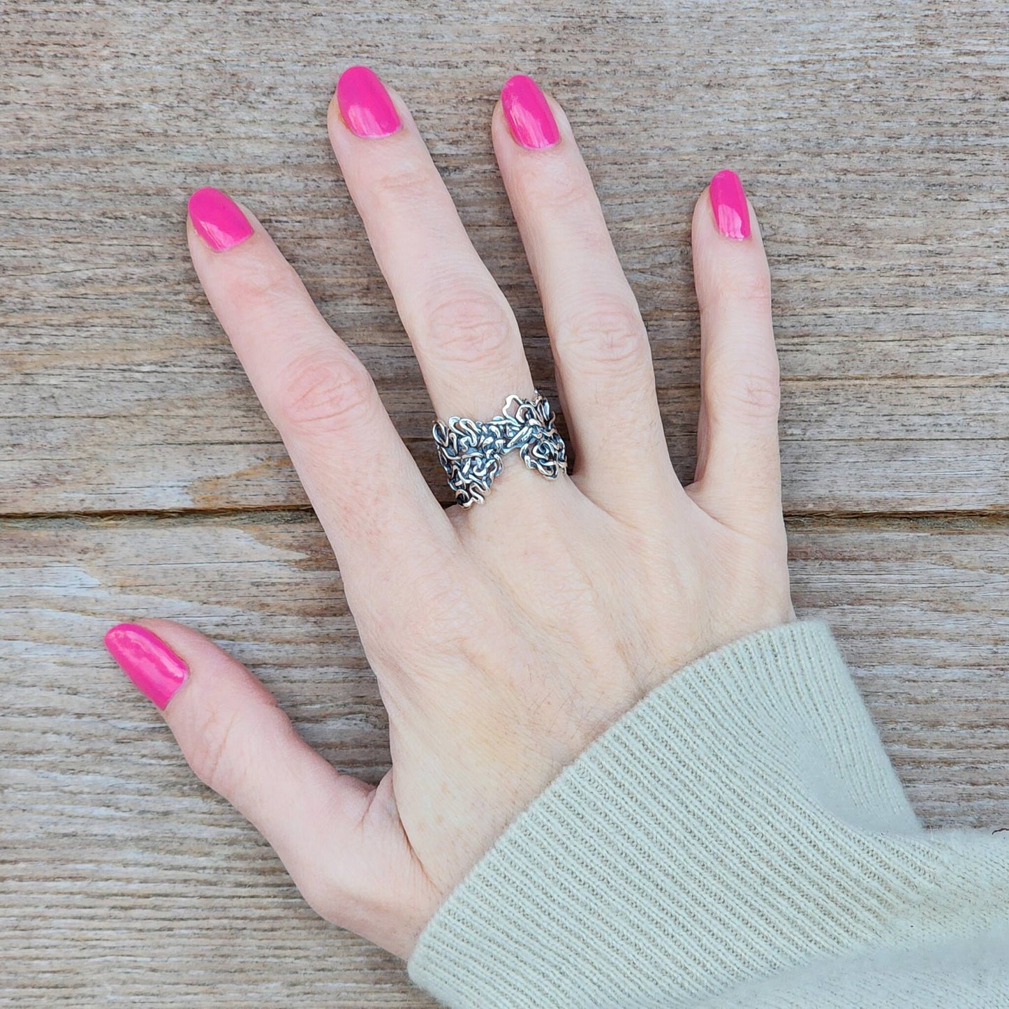 Hand with pink nail polish wearing a sterling silver calligraphic ring on a wooden surface