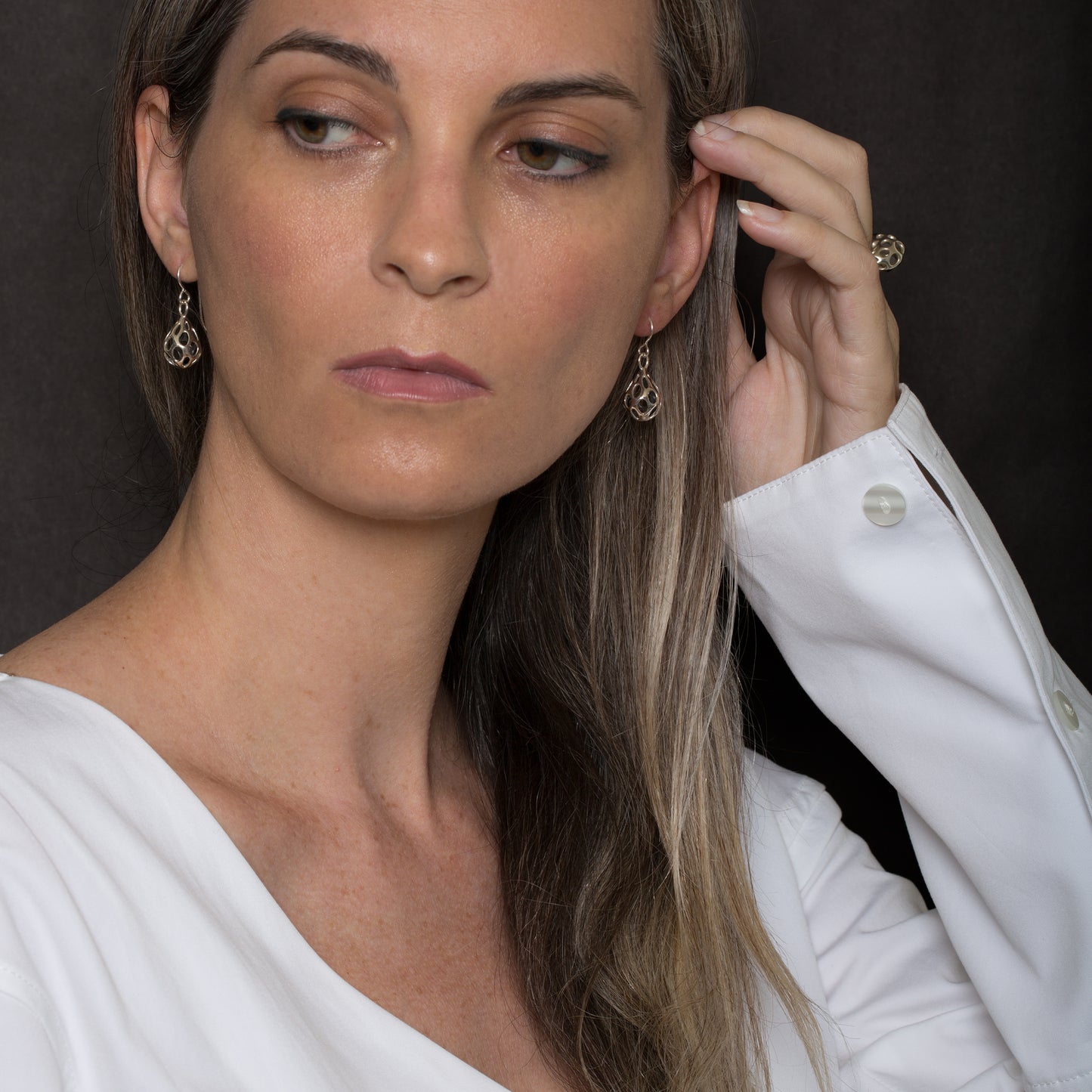 Xover0’s architectural OLEA drop earrings in polished sterling silver feature dimensional, sculptural latticework with elongated oval cutouts, paired with the matching ring worn on the model’s hand.