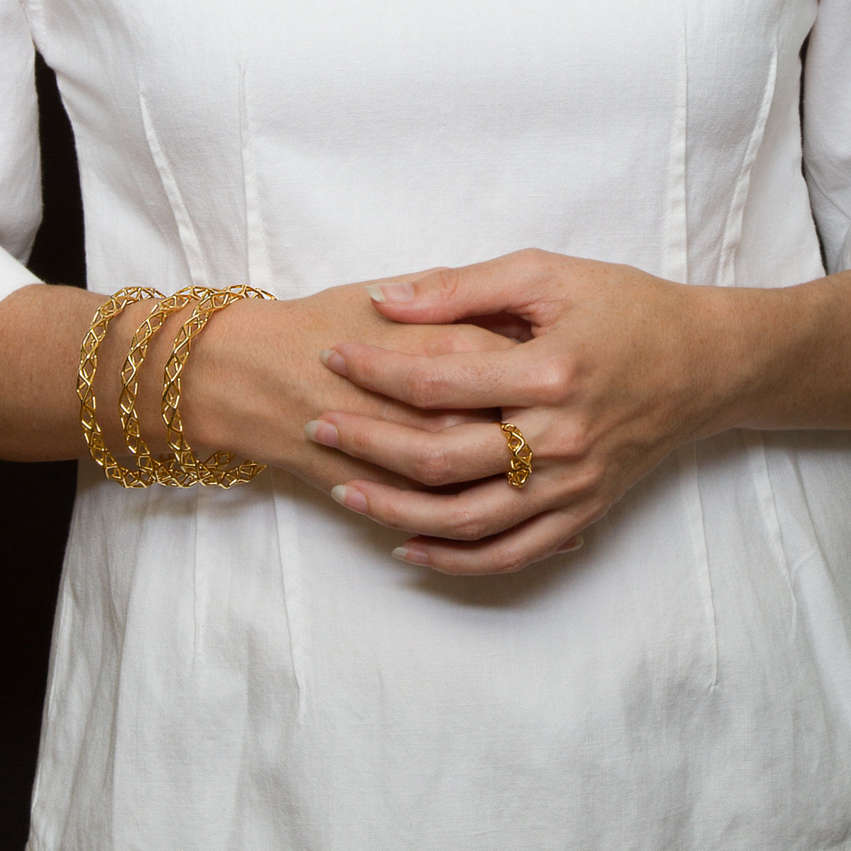 A person wearing a dynamic geometric ring and three matching bangle bracelets with the same abstract lattice design.