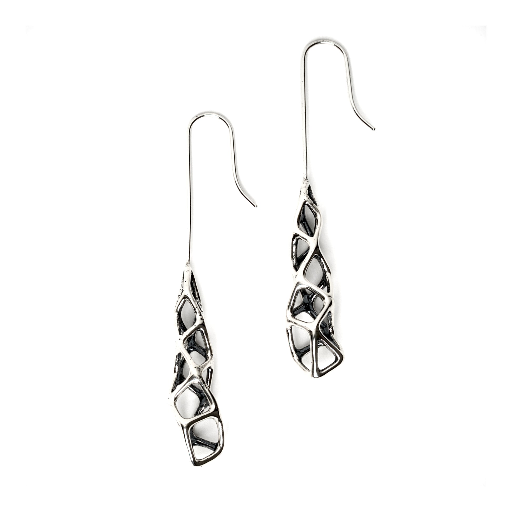 Edgy long drop dangle earrings in solid sterling silver are photographed with a macro lens on a white background. The extreme contrast is the result of blackening the recessed areas of the design with oxidation. The outer surfaces are polished to a mirror finish. The dimensional design emphasizes vertical length, gravity, and unconventional elegance. 