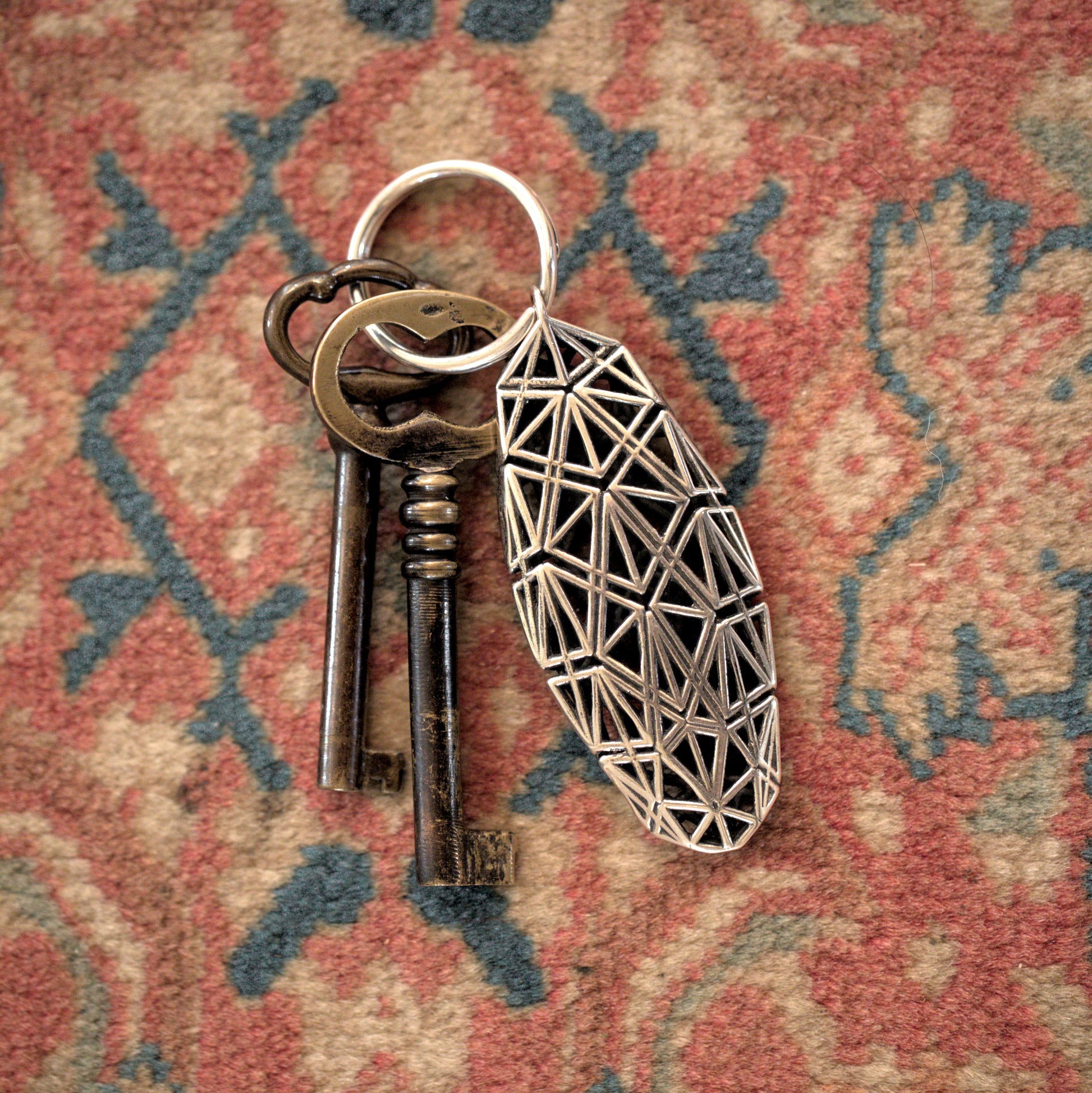 Sculptural sterling silver keychain featuring Art Deco-inspired lattice design secures antique keys. 