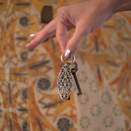 A woman's hand holding a bold sterling silver keychain defined by edgy dynamic geometry against a detailed precious metal background. 