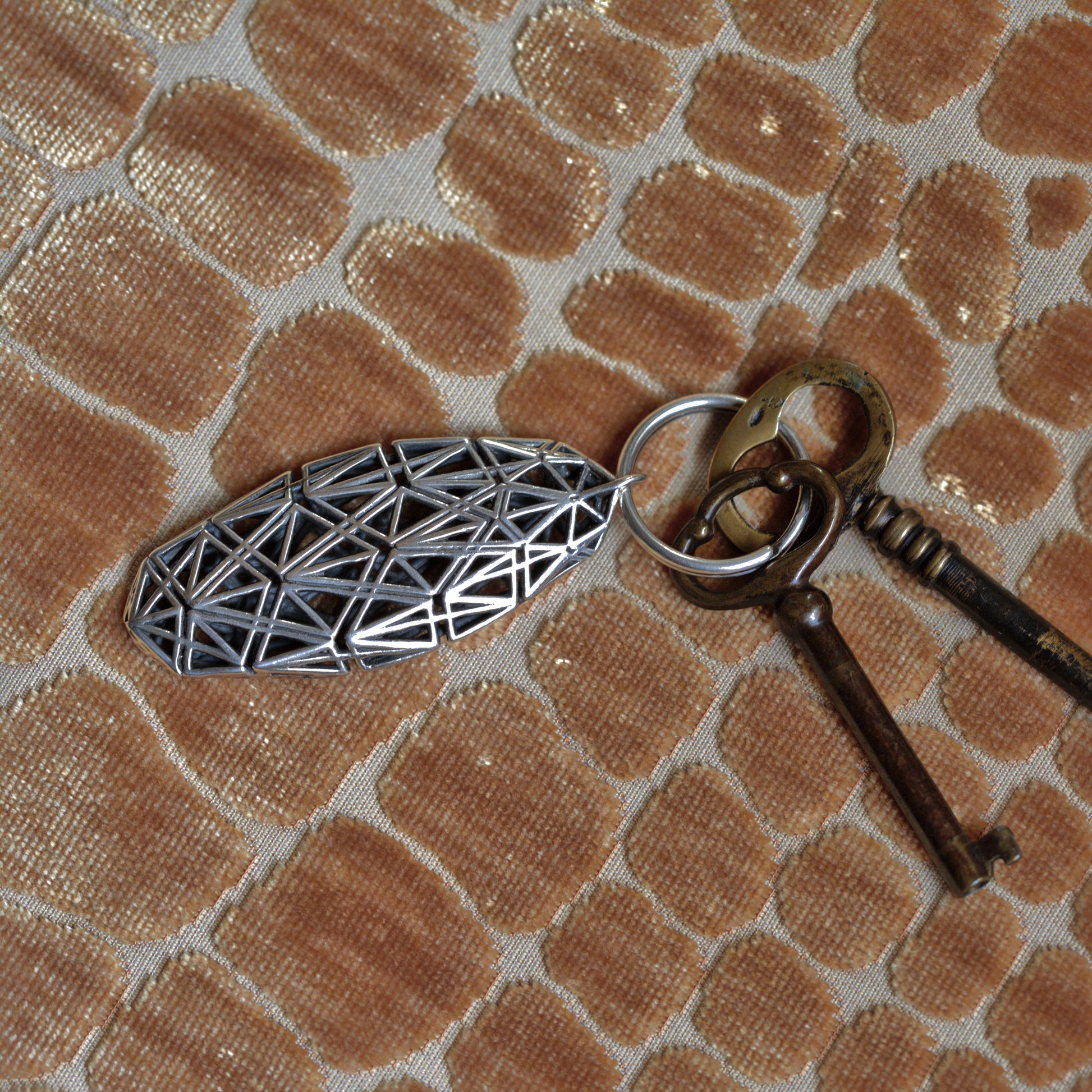 A sterling silver keychain with dimensional angular lattice pairs beautifully with richly patterned interiors in luxurious settings. Shown here with antique keys and velvet upholstery, this designer keychain complements well appointed interior decor. 