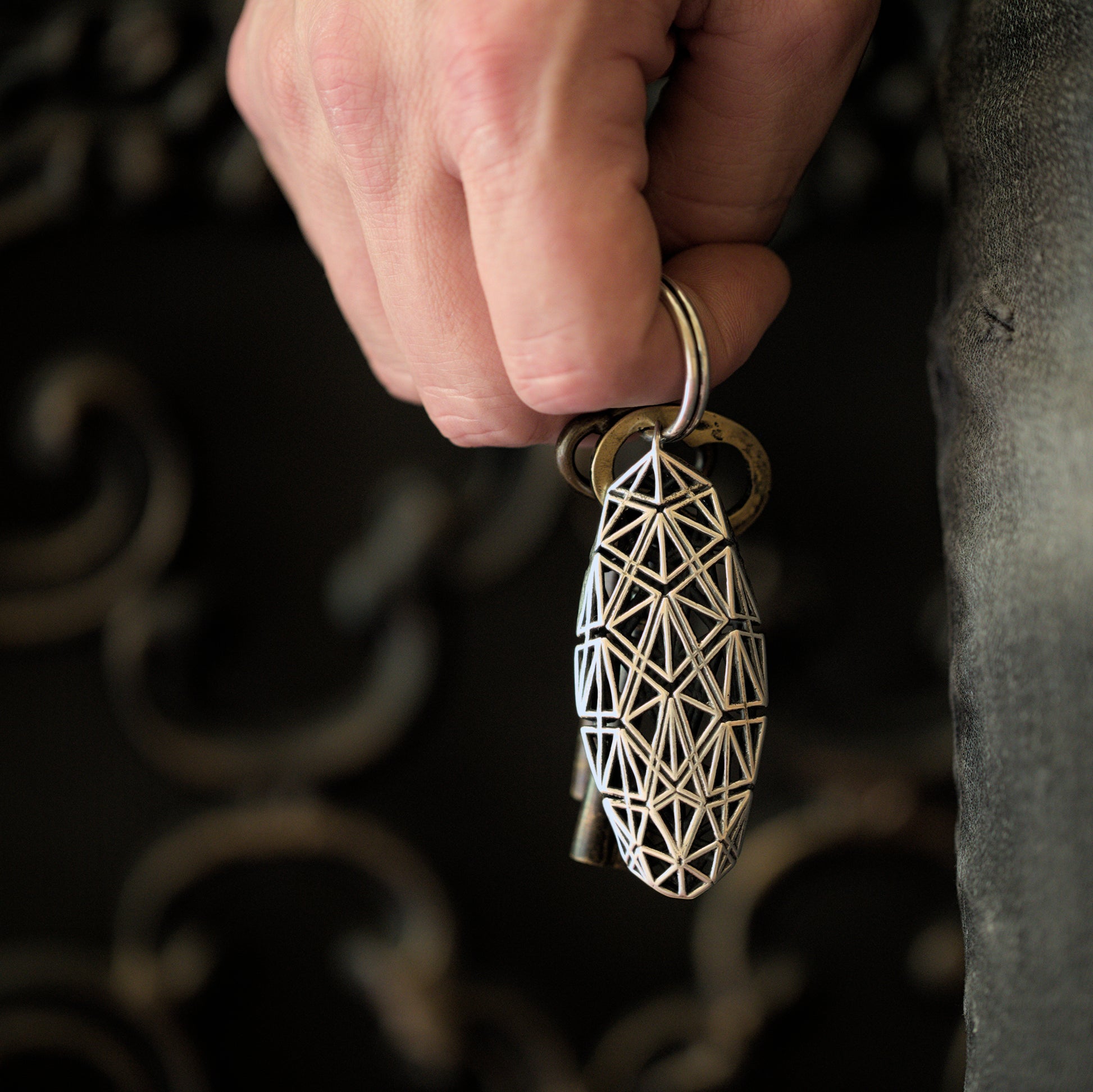 A sterling silver heirloom keychain with precise architectural details held in a man's hand. The richly patterned lattice design is easy to spot against any background.