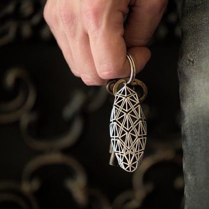 A sterling silver heirloom keychain with precise architectural details held in a man's hand. The richly patterned lattice design is easy to spot against any background.
